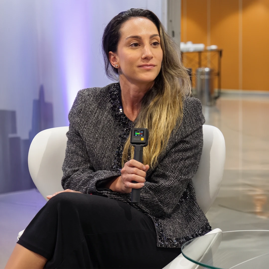 Dra. Thais Fonseca palestrando em evento, com terno tweed e microfone na mão